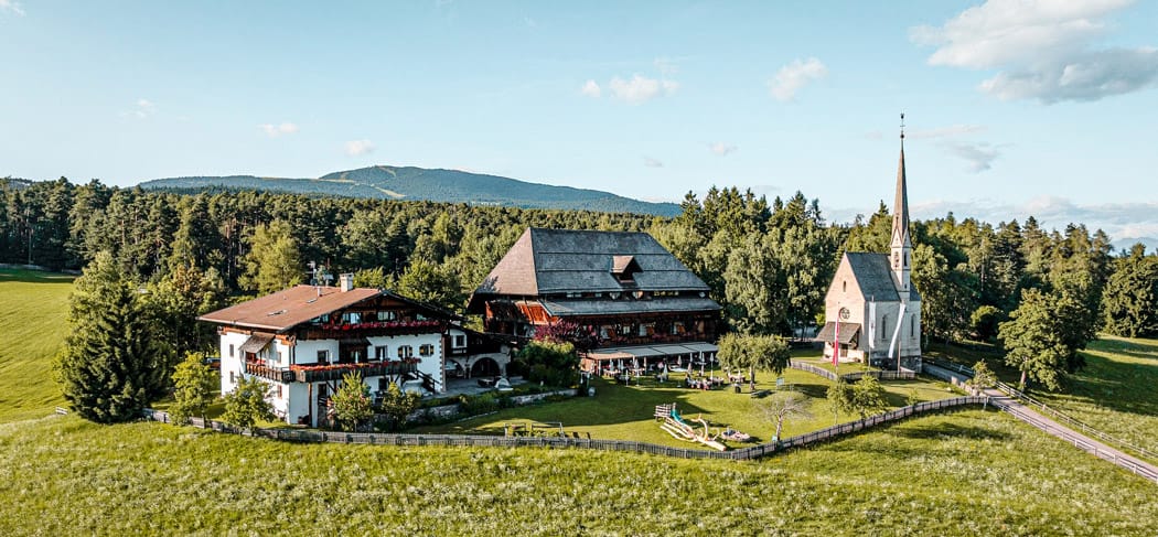 Ansitz Kematen presso Collalbo sul Renon con ristorante, hotel e piccola chiesa, circondato da prati e boschi, posizione soleggiata con vista panoramica sulle montagne dell'Alto Adige.