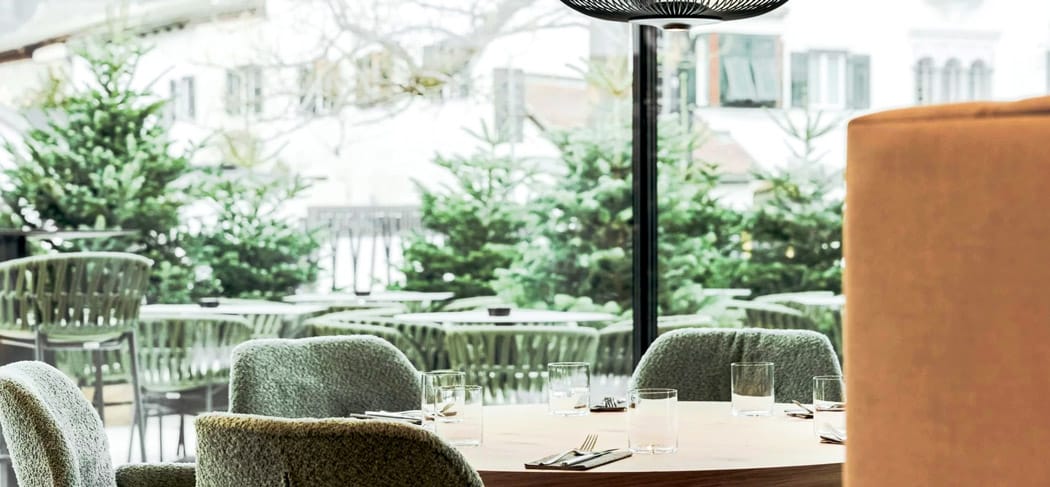 Elegantes Restaurant mit modernen grünen Sesseln, gedecktem Holztisch und Blick auf die Terrasse mit Tannen und Stadtfassaden im Soley Restaurant Brixen.