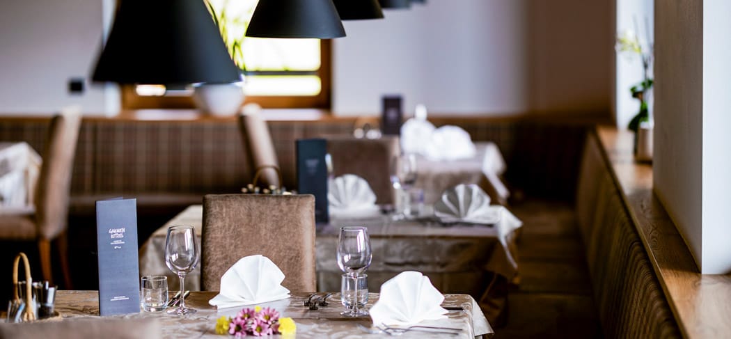 Tavoli elegantemente apparecchiati nel ristorante Rommisa a Vila di Sopra con tovaglioli in stoffa, calici e luce calda in un’atmosfera accogliente.