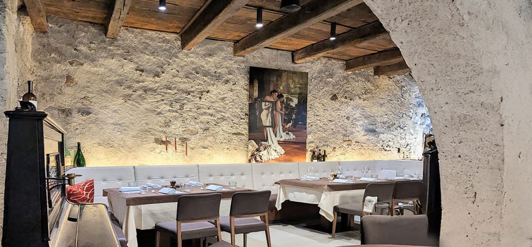 Sala storica del ristorante Festival Merano con pareti in pietra naturale, soffitto in legno, opere d'arte moderna e tavoli apparecchiati in un'atmosfera elegante e accogliente.