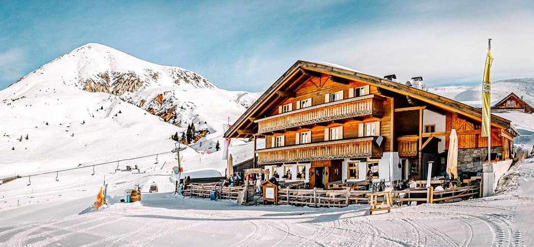 Die Kirchsteiger Alm bei Meran 2000 mit Sonnenterrasse und Schnee – umgeben von Skipisten, verschneiten Wegen und Gipfeln, ideal für Wanderer und Skifahrer.