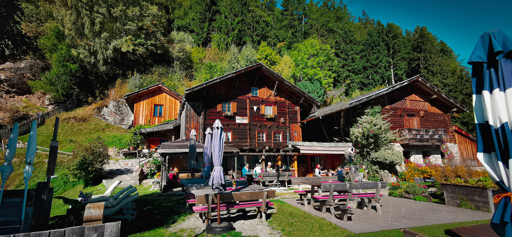 Gemütliche Jausenstation Naserhof im Kalmtal bei St. Martin in Passeier mit sonniger Terrasse, blühendem Garten und traditionellem Holzbau vor beeindruckender Bergkulisse.