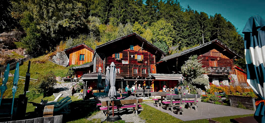 Gemütliche Jausenstation Naserhof im Kalmtal bei St. Martin in Passeier mit sonniger Terrasse, blühendem Garten und traditionellem Holzbau vor beeindruckender Bergkulisse.