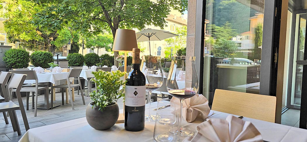 Elegant gedeckter Tisch mit Rotwein, Gläsern und Deko auf der Terrasse des Weinbistro Gries 13 in Bozen – stilvolles Ambiente unter Bäumen am Grieser Platz.