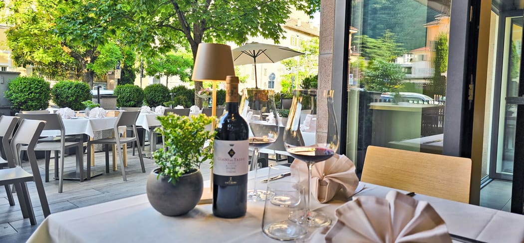 Elegant gedeckter Tisch mit Rotwein, Gläsern und Deko auf der Terrasse des Weinbistro Gries 13 in Bozen – stilvolles Ambiente unter Bäumen am Grieser Platz.