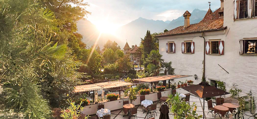 Romantische Terrasse des Restaurants Castel Rundegg in Meran mit Blick auf Berge und Garten – perfekter Ort für Dinner bei Sonnenuntergang in Südtirol.