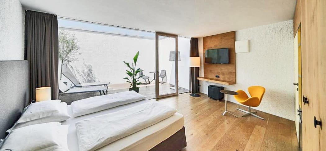 Modern eingerichtete Suite im Soley Suites Hotel in Brixen mit Holzfußboden, Designmöbeln, TV, privater Terrasse und Liegestühlen – stilvoller Rückzugsort im Eisacktal.