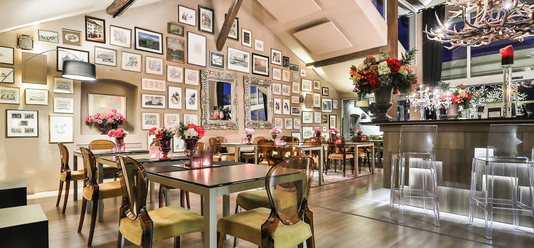 Arôme Ristorante & Caffè a Bolzano: ambiente raffinato con pareti a galleria, tavoli eleganti, decorazioni floreali, bar moderno e illuminazione accogliente