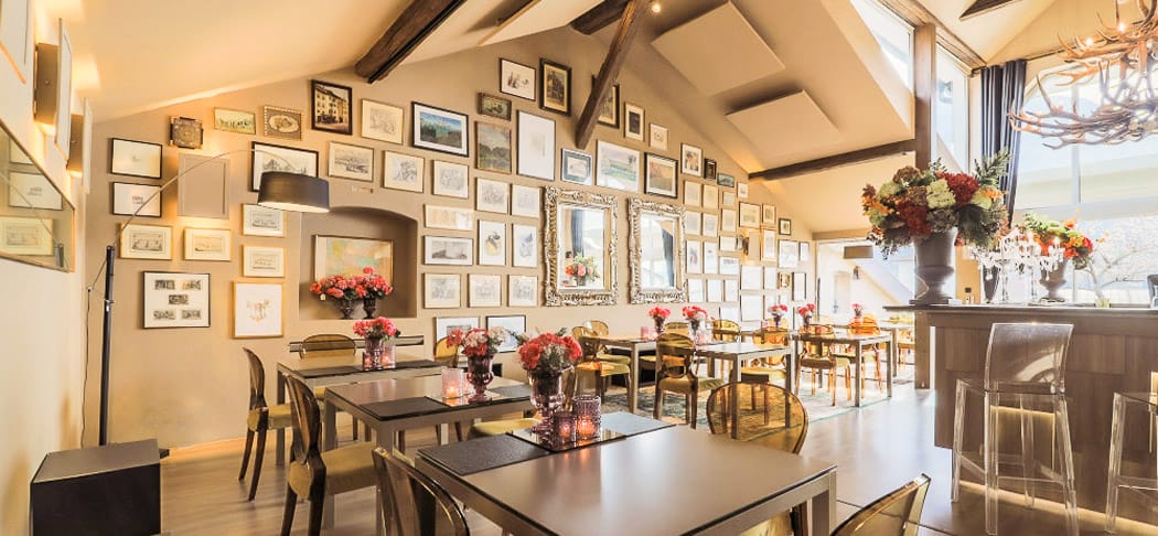 Arôme Ristorante & Caffè a Bolzano: ambiente raffinato con pareti a galleria, tavoli eleganti, decorazioni floreali, bar moderno e illuminazione accogliente
