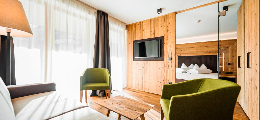 Camera luminosa dell'Hotel Adlernest nella Val Senales con legno naturale, accogliente angolo salotto, poltrone moderne, letto grande e finestre a tutta altezza.