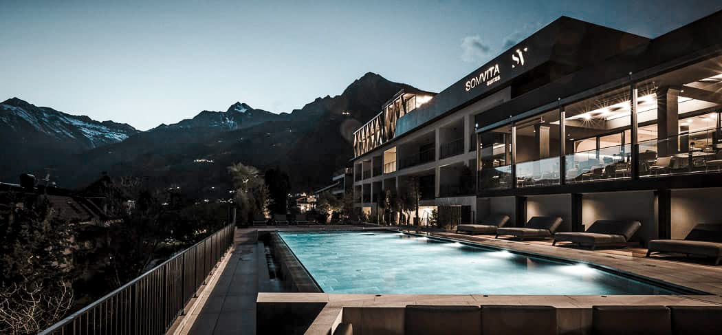 SomVita Suites a Tirolo di notte, con piscina a sfioro, moderna area benessere e una vista panoramica da sogno sulle montagne dell'Alto Adige.