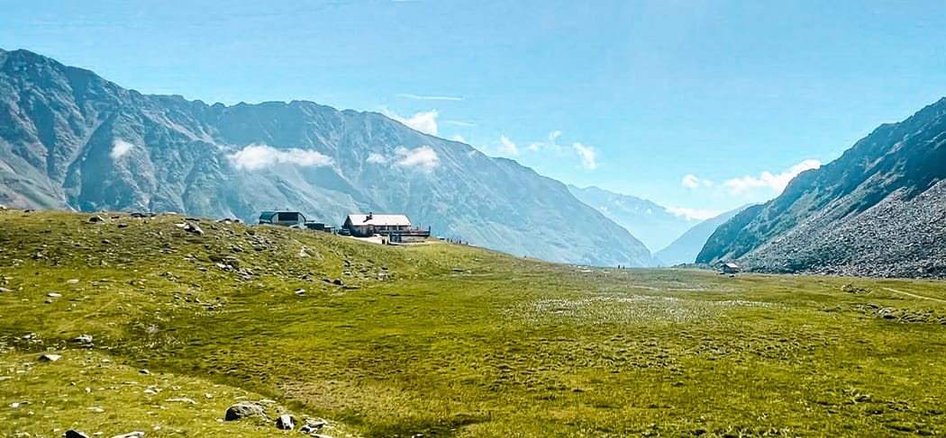 Ampi prati alpini sull'altopiano del Lazaun nella Val Senales, vista sul Rifugio Lazaunhütte immerso nel verde paesaggio alpino e circondato da ripidi versanti montuosi.