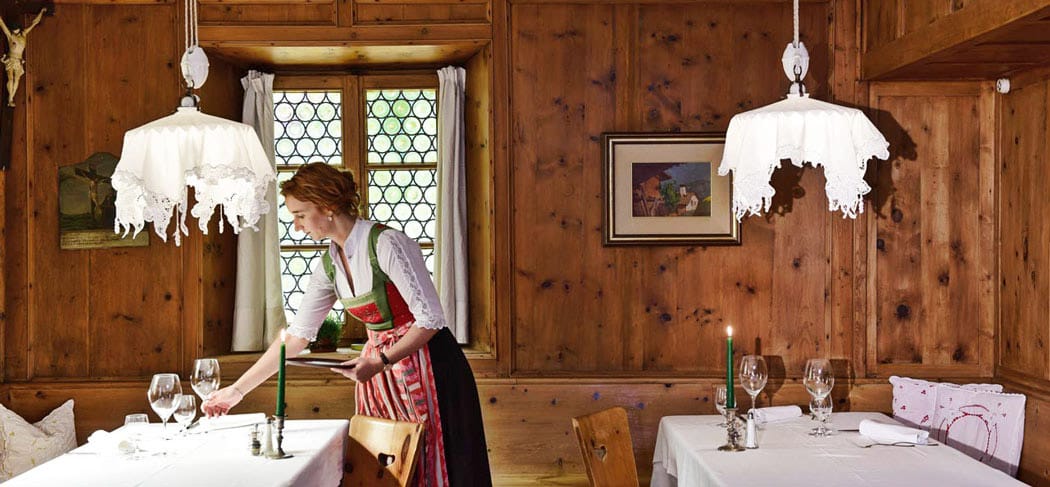 Maria im Dirndl deckt einen Tisch in der gemütlichen Holzstube des Restaurants Turmwirt in Gufidaun – traditionelles Ambiente, Kerzenlicht und Südtiroler Gastlichkeit.