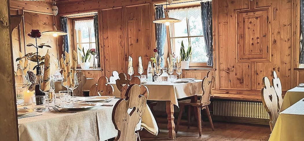 Accogliente stube rivestita in legno nell'osteria contadina Oberpartegger a Villandro con tavoli apparecchiati con cura, luci calde e vista sul paesaggio montano dell'Alto Adige.