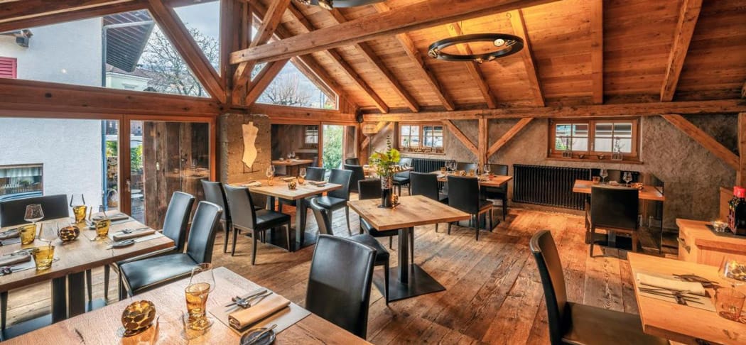 Blick in das Restaurant & Weinlounge Stadele in Lana in Südtirol mit ansprechendem Speisesaal in Holz, hohen Fenstern und alten Mauern.