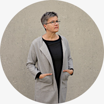 Porträt von Uschi Holstein, stehend vor einer Wand, den Blick leicht seitlich nach oben gerichtet, in sich ruhend und gelassen