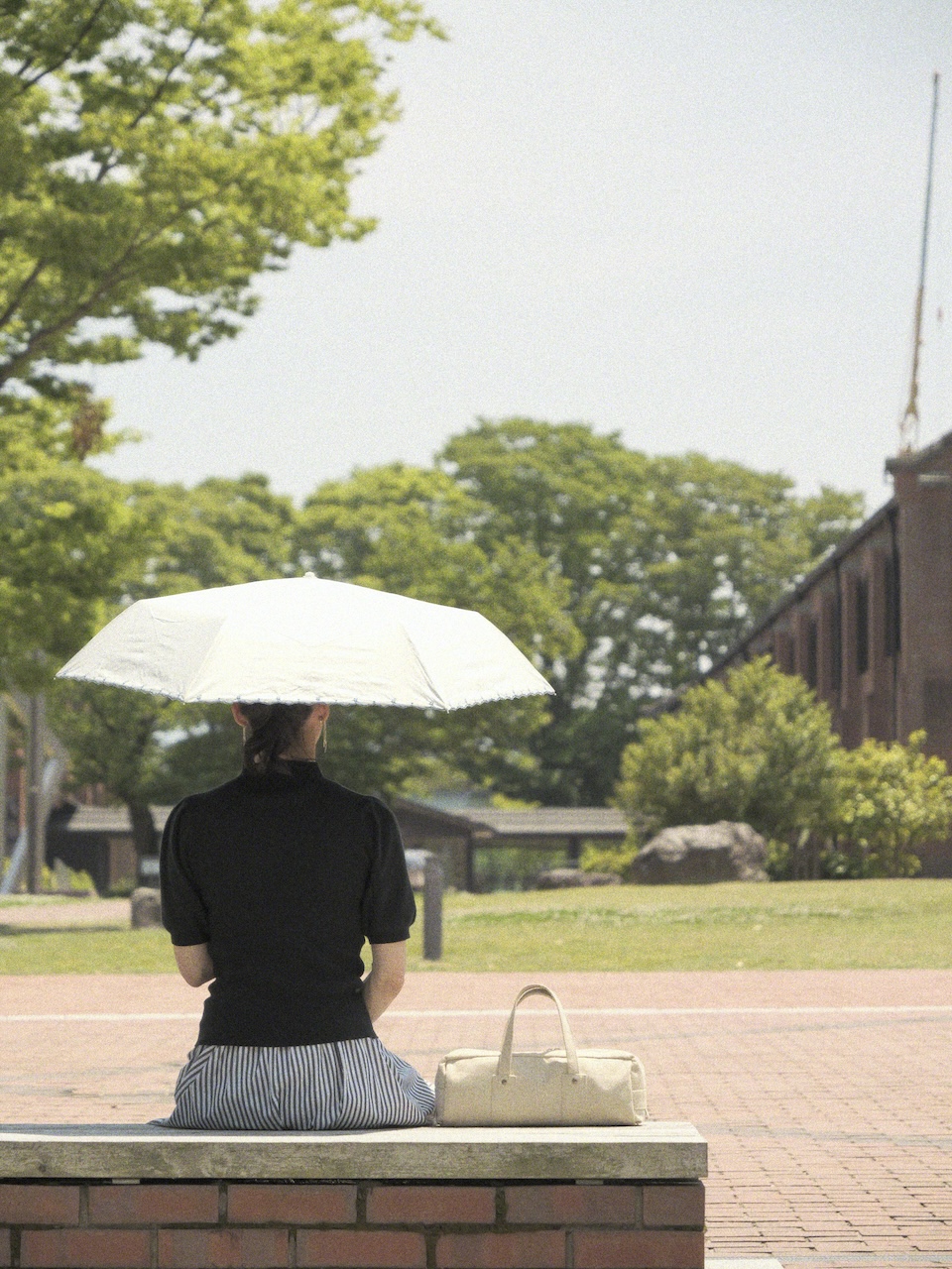 超横長ボストンバッグは可愛らしくシンプル。でも大容量のおしゃれなバッグを日傘をさした女性と共にベンチに腰掛けた後ろ姿の写真