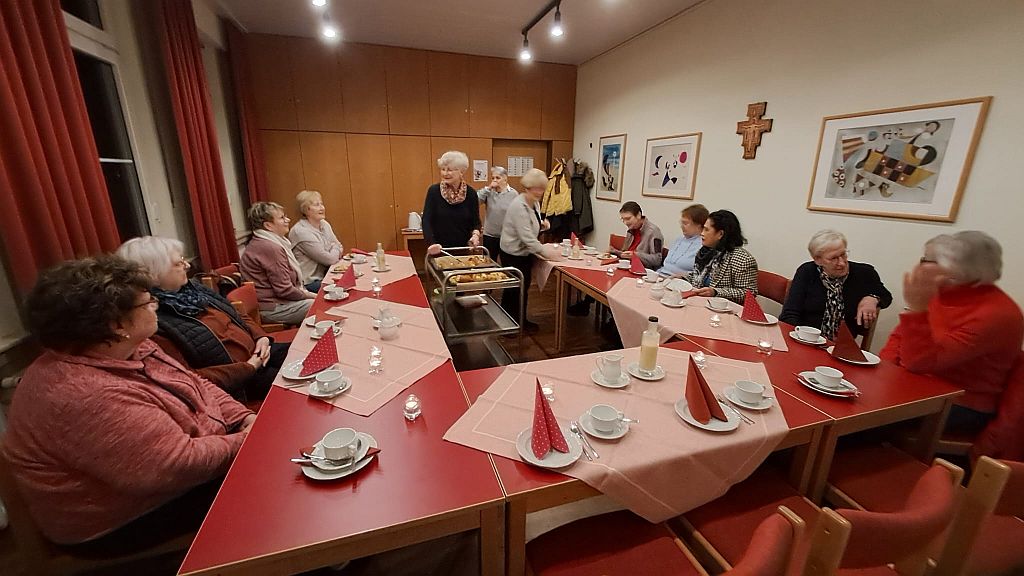 Foto zeigt die Gruppe der kfd-Frauen an einem Tisch in U-Form. Sie warten darauf, dass die frischen Bratäpfel serviert werden.