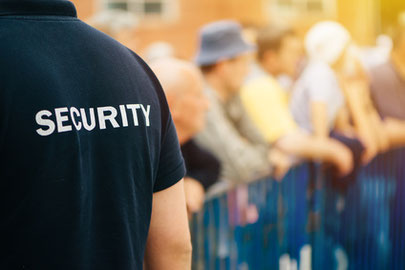 Sicherheits-Mitarbeiter mit Schriftzug "SECURITY"auf dem Rücken vor Straßen-Absperrung, ggf. auch im Stadion oder bei einem Konzert.