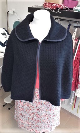 Capeline en lainage aspect gaufré, bordée d'un biais de coton. Elle s'attache à l'aide d'un petit crochet.