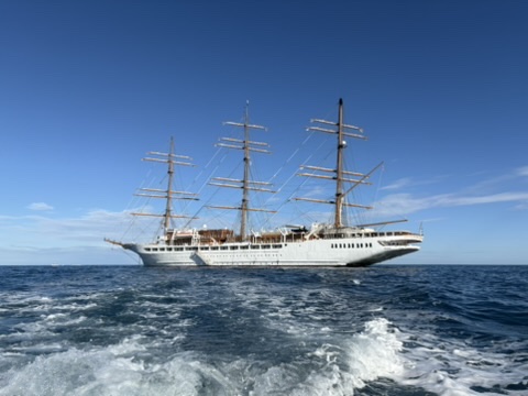 Segelschiff Sea Cloud ohne gesetzte Segel auf dem Mittelmeer, fotografiert hinter dem Wasserwirbel eines Tenderboots unter klarem Himmel.