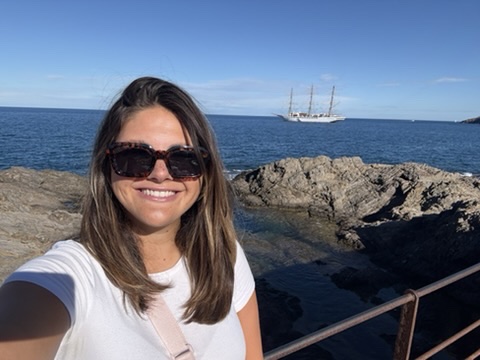 Anne Kessenich an einer Felsküste mit Blick auf die Sea Cloud Spirit, einem historischen Windjammer auf Segelkreuzfahrt im Mittelmeer.