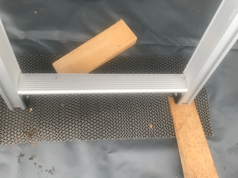 Holzkeil zum Ausgleichen der Schräge und Schutzmatte zum Schutz des Zeltbodens unter der Klappleiter.