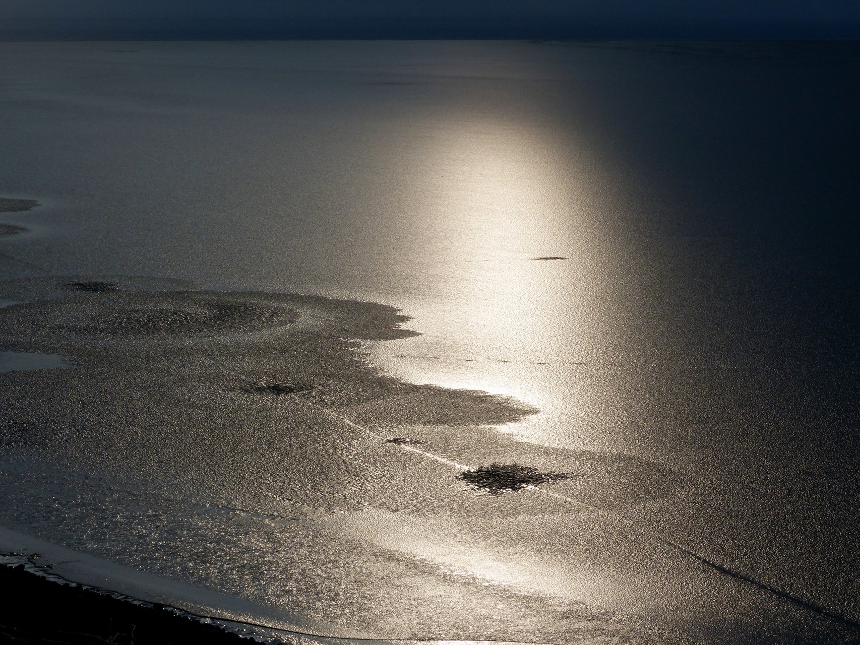 Die aufgehende Sonne spiegelt sich im dünnen Eis des See's