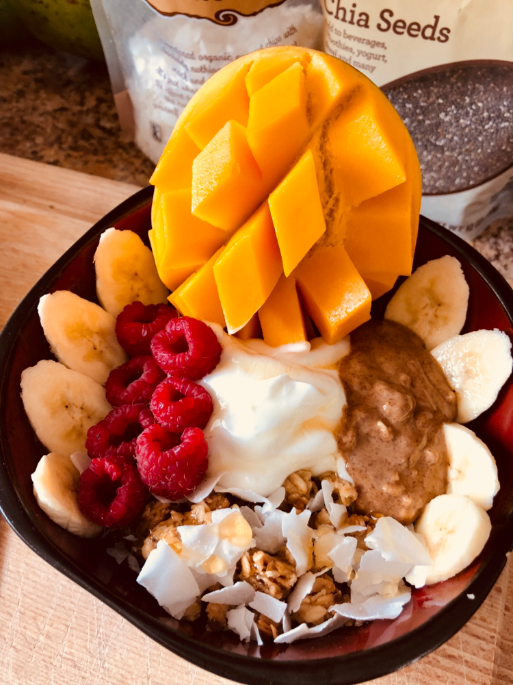 Self-made Açaí Bowl, decorated with my favorite toppings: raspberry, coconut chips, banana, mango, honey granola, mango, raw almond butter and Greek yogurt.