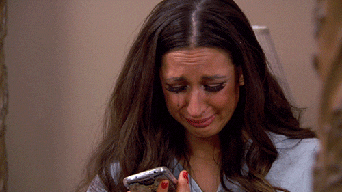 Actrice brune en pleurs, son mascara coule sur ses joues et elle tient un téléphone portable dans sa main.