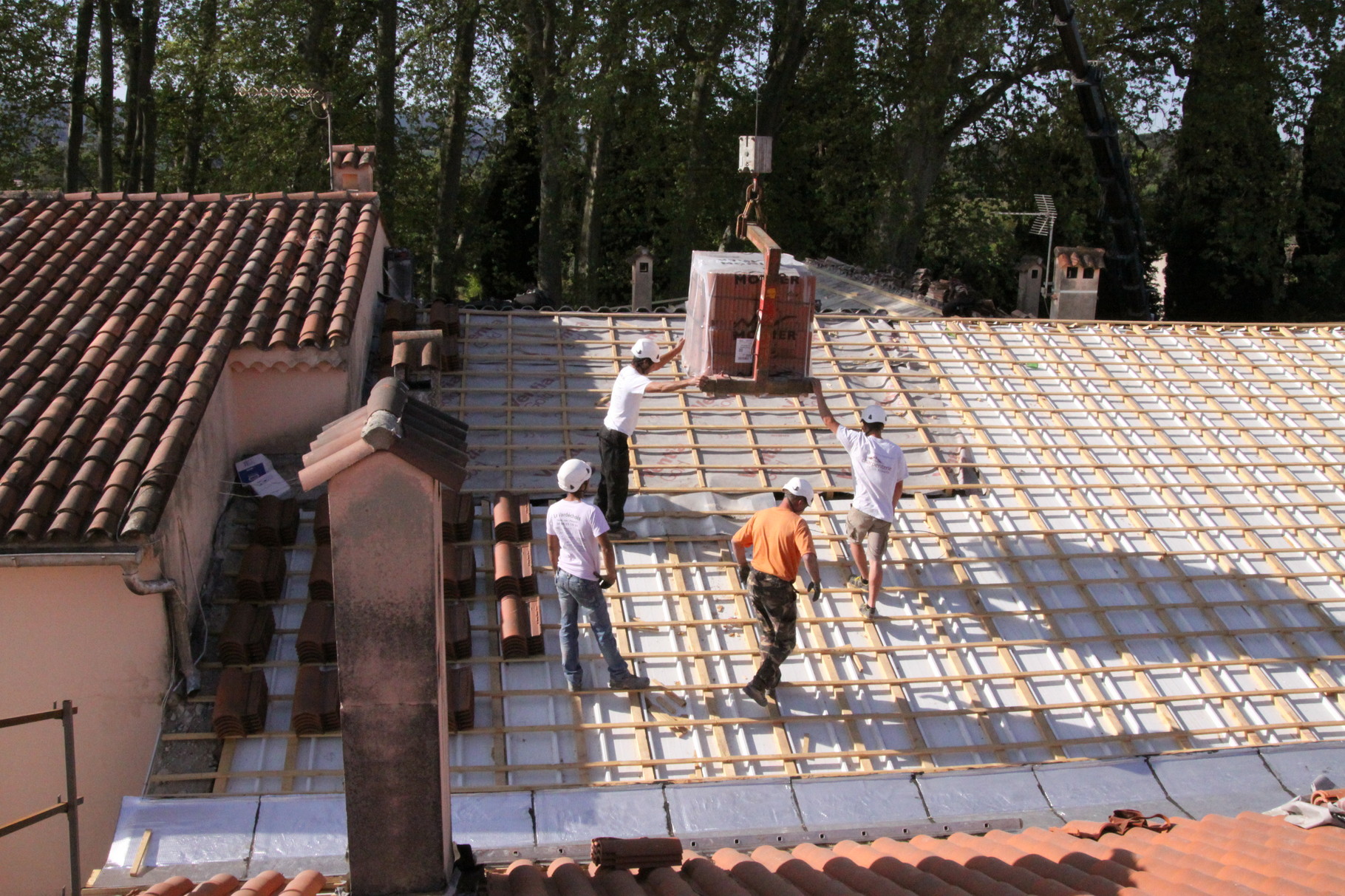 dépose des palettes de tuiles sur le toit avec une grue 