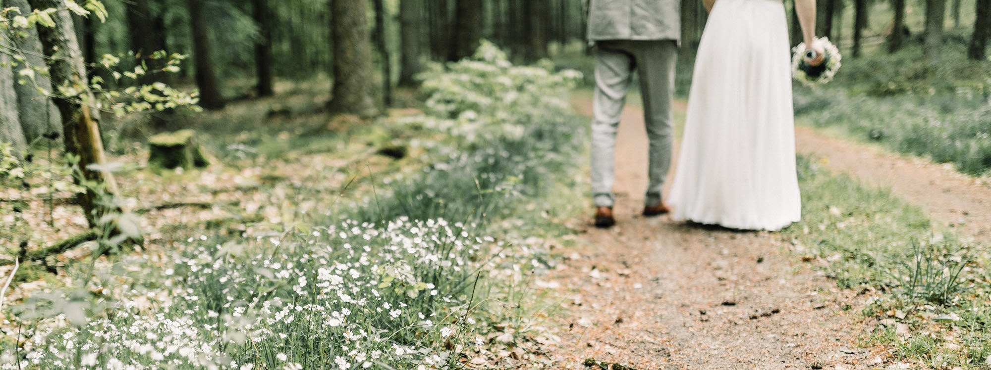 Hochzeitspaar läuft auf einem Waldweg, Blumen wachsen am Wegesrand