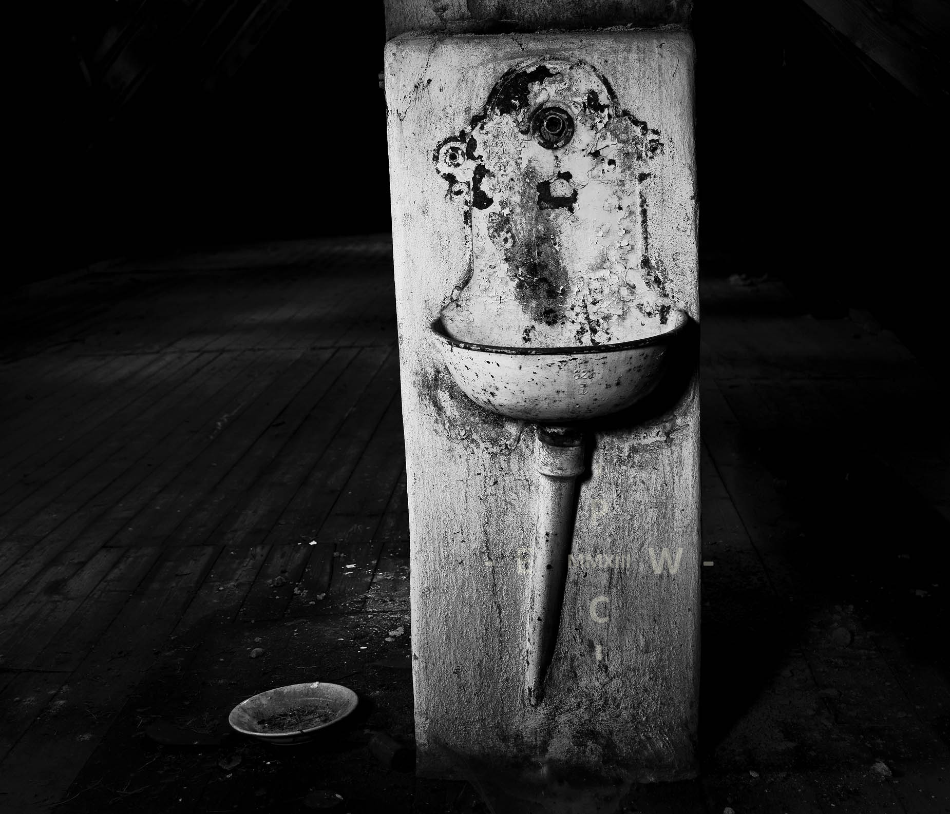 Grafische Schwarz-Weiß-Aufnahme eines alten Waschbeckens in der Mitte eines dunklen Raumes