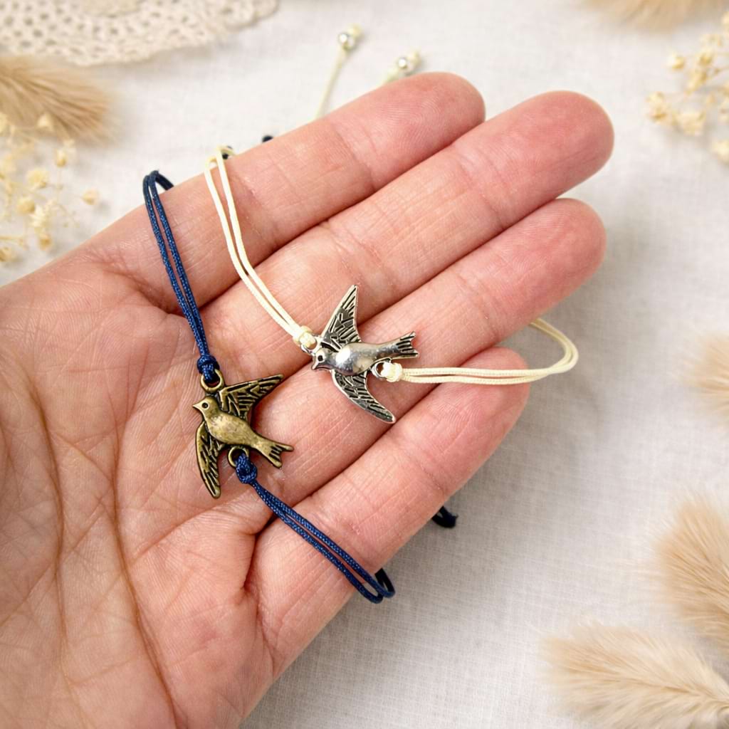 Zwei Makramee‑Armbänder mit Vogelanhängern in der Hand.