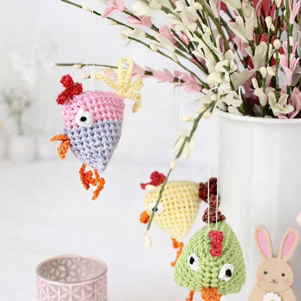 Bunte gehäkelte Vogelanhänger als handgemachte Osterdeko, arrangiert an Zweigen.