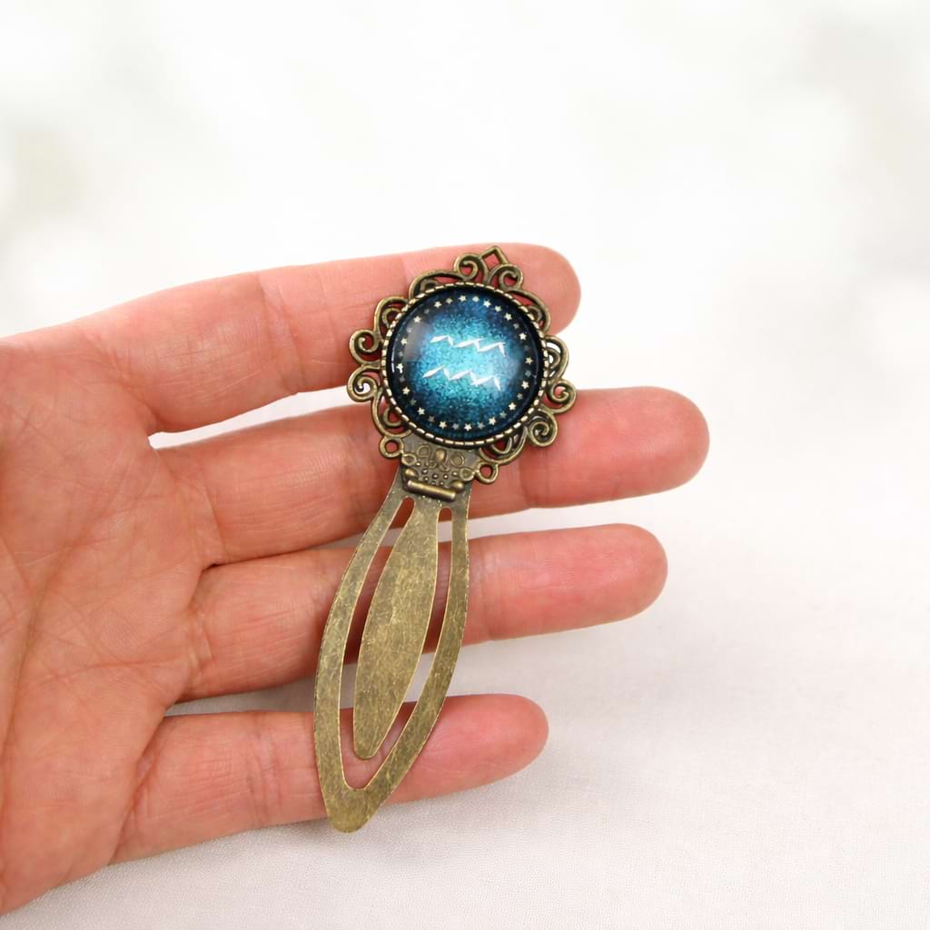 Filigranes Aquarius‑Sternzeichen‑Lesezeichen aus Metall mit blauem Cabochon, handgefertigt als persönliches Geschenk für Leseratten.