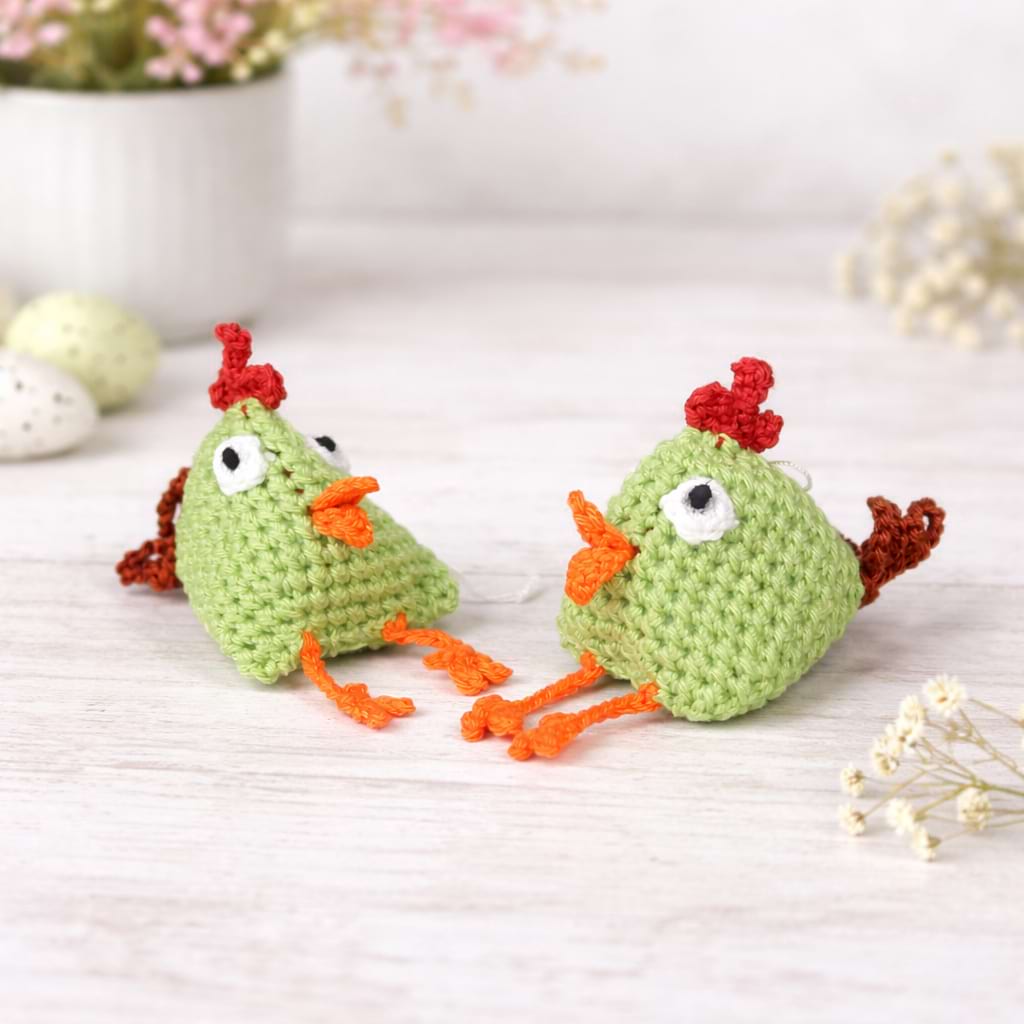 Gehäkelte grüne Mini-Hühner als handgemachte Osterdeko, dekoriert mit Frühlingsblumen und Eiern für Produktpräsentation.