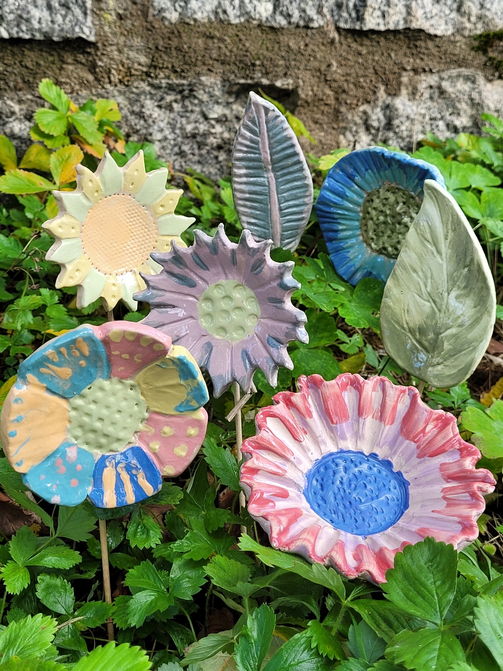 mehrere bunt bemalte Blüten, Federn, Blätter aus Ton auf Holzstäben