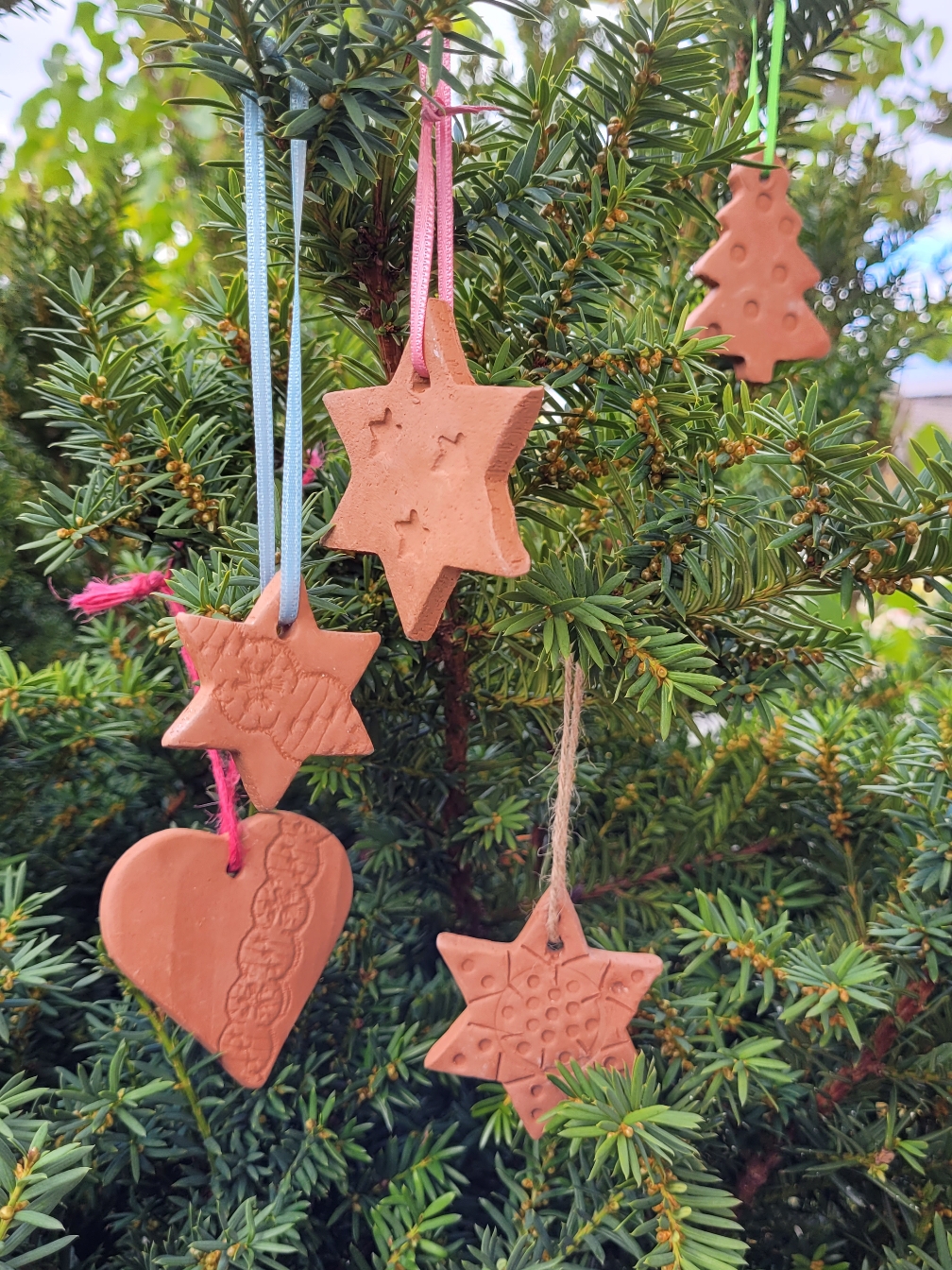 verschiedene weihnachtliche Formen aus rotbraunem Ton an Tannenbaum hängend