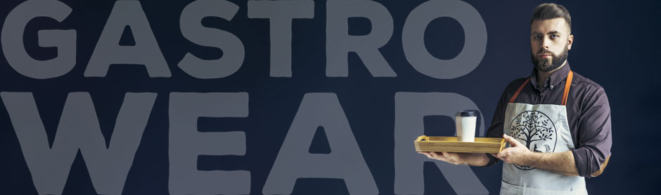 Mann mit Bart trägt eine Schürze mit Baumlogo und hält ein Tablett mit Kaffeebecher vor dunkelblauem Hintergrund mit dem Schriftzug „GASTRO WEAR“.