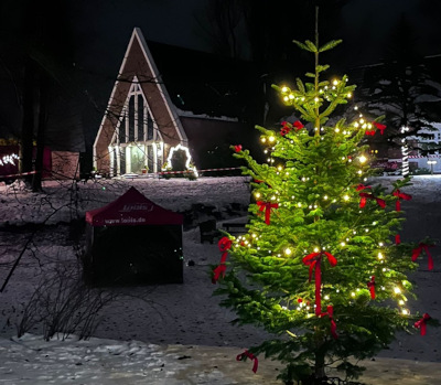 geschmückter Weihnachtsbaum mit Lichterkette vor einer Kirche