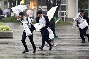 強い風と雨に飛ばされそうになって道路を渡る人々。