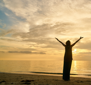 Eine Person steht im Abendlicht am Strand und reckt sich entspannt dem Wasser entgegen. Ganz gleich, welche Herausforderung auf die Person zukommt. Sie fühlt sich gewappnet - resilient in Schicksalsmomenten und Stress. Martina Reichl