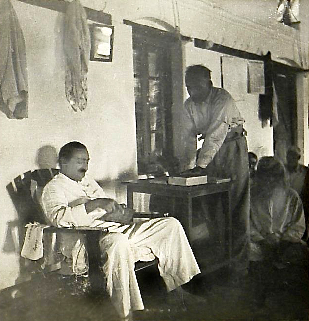 Baba seated in Lower Meherabad mandali hall giving instructions on his alphabet board with Dr Ghani standing & writing it down, at the New Life meeting - Photo taken by Padri 