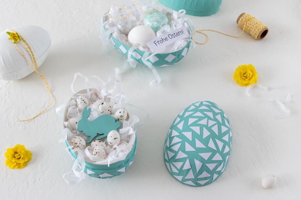 Papp-Ei als DIY-Osterüberraschung gefüllt mit weissem Ostergras und Marzipaneiern Osterhase aus Holz dekoriert mit gelben Primeln