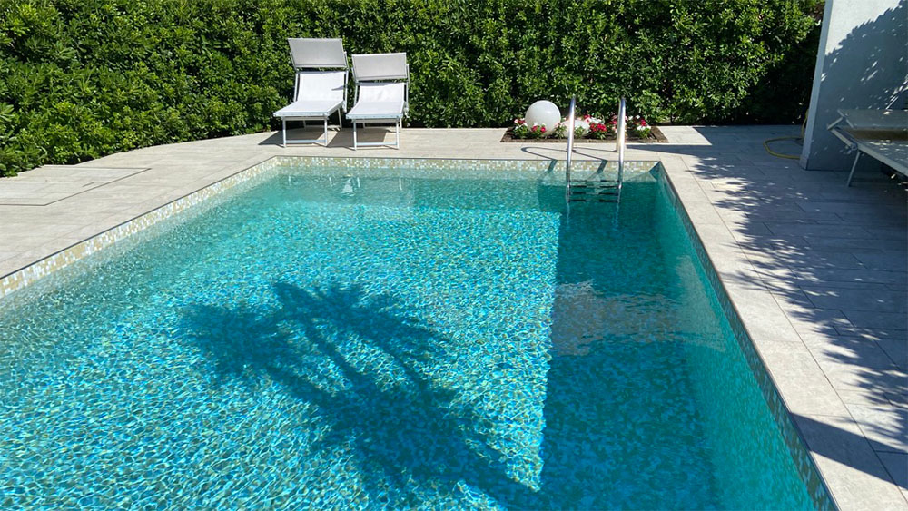 Ein kleiner Pool mit einer Palme in der Mitte, umgeben von grünem Gras und einem klaren blauen Himmel.