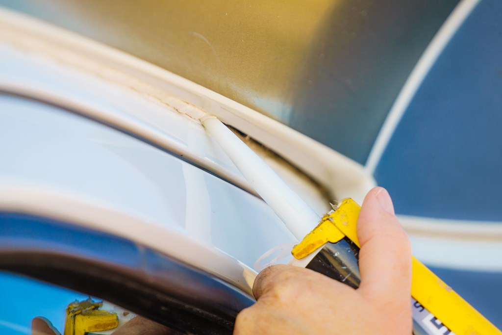 Eine Person trägt Silikondichtstoff von Hand an den Kanten eines Wohnwagens auf. Ein Mann überprüft und ersetzt die Dichtungen des Wohnmobils.