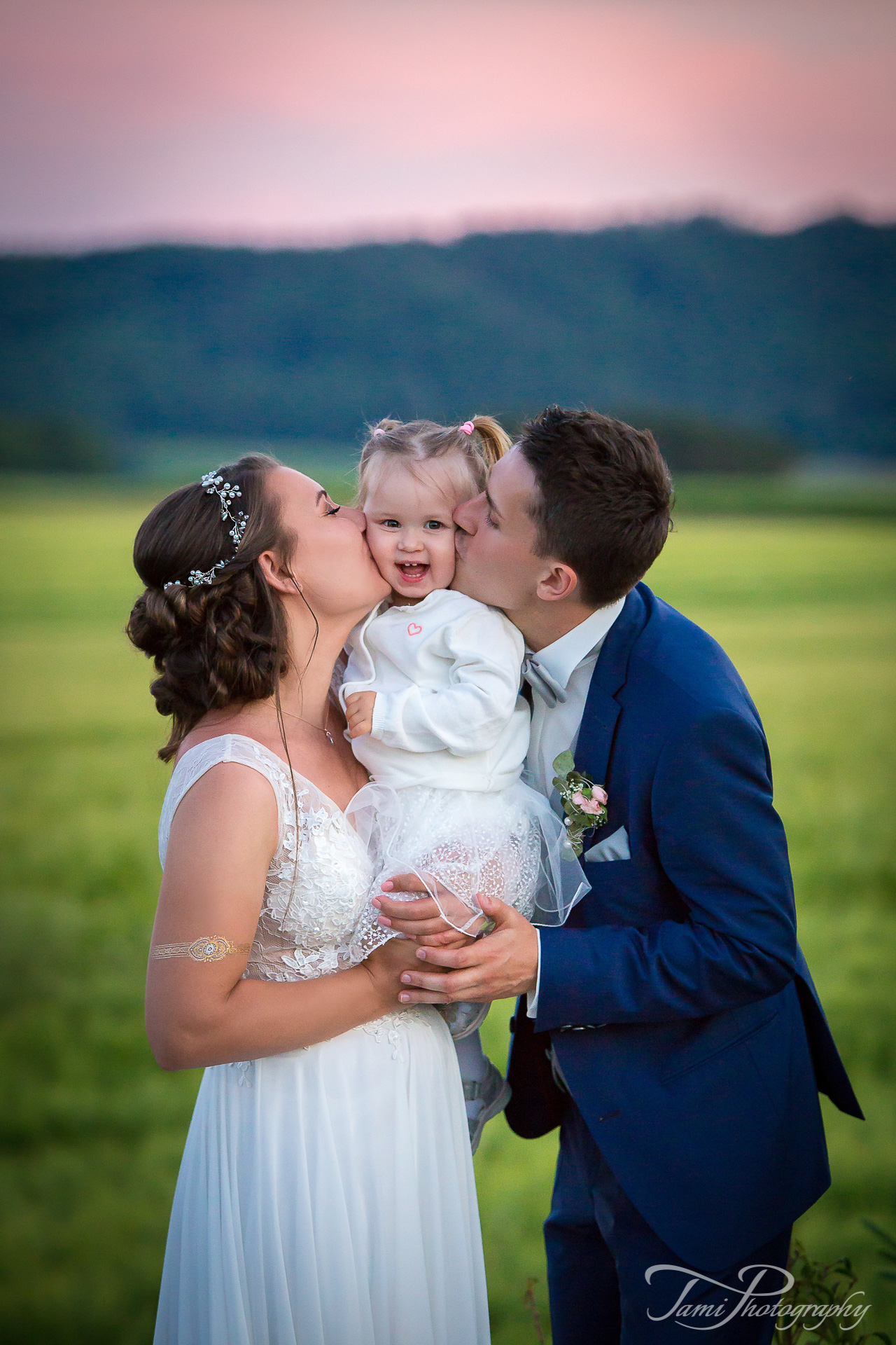 Familienfotografie nach der Taufe und Hochzeit im Freien mit Küssen der Eltern auf beiden Seiten
