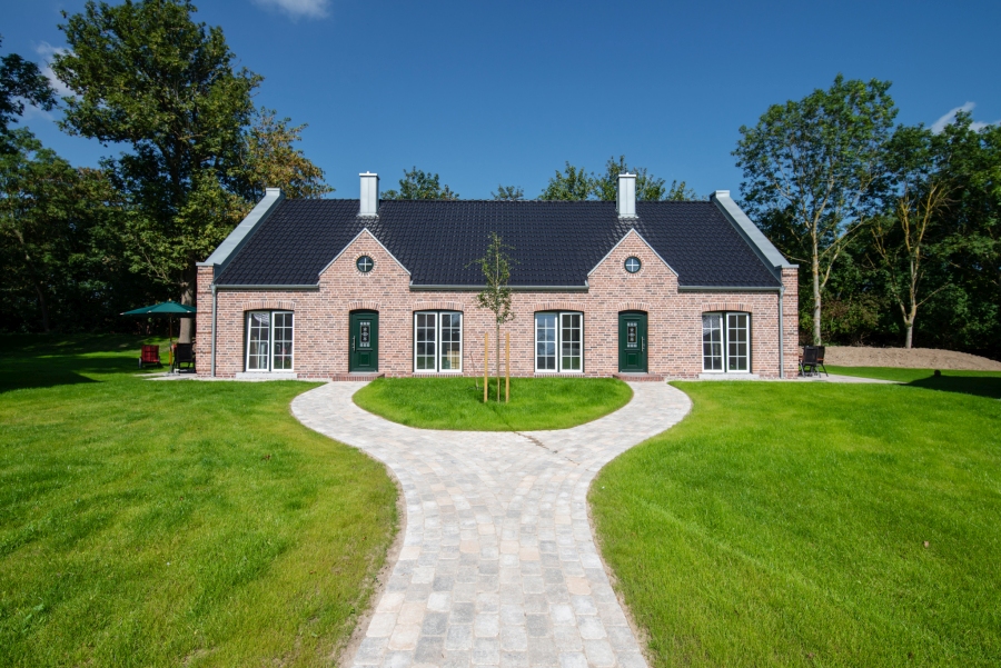 Klassisches Backstein-Doppelhaus in Rot mit großen Fenstern und symmetrischem Design, das zwei hochwertige Ferienwohnungen beherbergt.