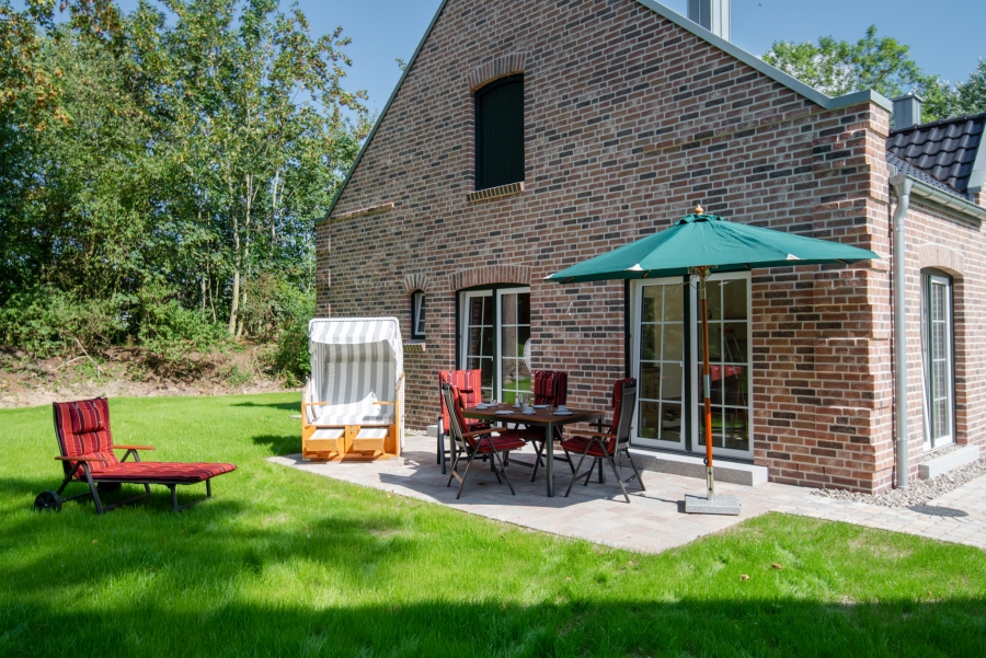 Typisch norddeutsches Ferienhaus aus rotem Backstein mit gemütlichem Außenbereich, Gartenmöbeln und einem weißen Strandkorb im Grünen.